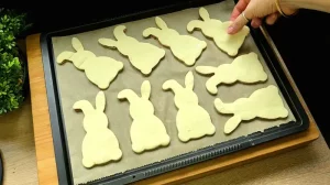 Ausgestochene Blätterteig-Hasen liegen bereit auf einem Backblech mit Backpapier vor dem Backen
