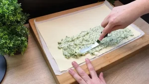 Eine cremige Bärlauch-Käse-Masse wird gleichmäßig auf die untere Hälfte des Blätterteigs gestrichen.