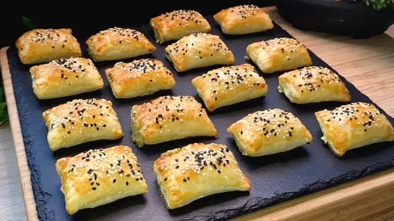 Goldbraun gebackene Blätterteig-Häppchen mit Bärlauch-Käse-Füllung und Sesam-Bestreuung.