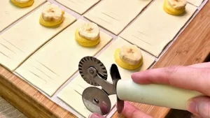 Eine Bananenscheibe liegt auf dem Pudding, daneben sind kleine Schnitte im Blätterteig für das Muster zu sehen.