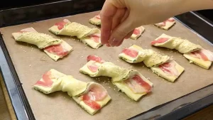 Hände, die einen mit Speck belegten Blätterteigstreifen spiralförmig drehen, um die Twister-Form zu erhalten.