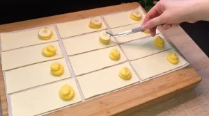 Ein Löffel cremiger Vanillepudding wird auf kleine Blätterteig-Rechtecke gesetzt.