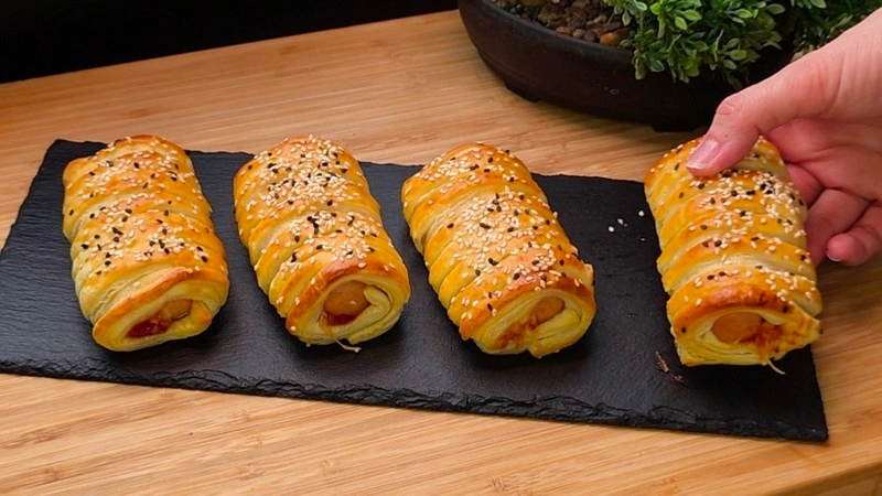 Goldbraun gebackene Blätterteig Hot-Dogs mit Sesambestreuung auf einem Teller.