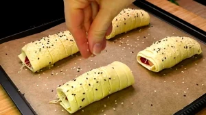 Blätterteig-Rollen werden vor dem Backen mit Sesambestreuung versehen.