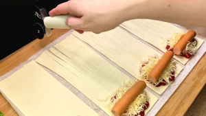 Ein Messer schneidet kleine parallele Schlitze in den Blätterteig, um ein Muster zu erzeugen.