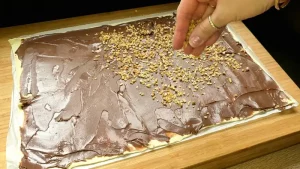 Eine Schicht Blätterteig wird großzügig mit Nutella bestrichen und mit gehackten Haselnüssen bestreut.