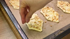 Gehackte Haselnüsse werden auf den mit Ei bestrichenen, rohen Blätterteig vor dem Backen gestreut.