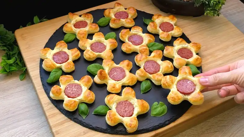 Goldbraun gebackene Blätterteigblumen belegt mit Kräuterfrischkäse, Käse und Cabanossi-Scheiben