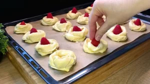 Eine Hand platziert vorsichtig eine frische Himbeere in die Mitte der vorbereiteten Teig-Schnecken.