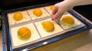 Gehobelte Mandeln werden auf den mit Ei bestrichenen Rand des Blätterteigs neben dem Pfirsich gestreut.