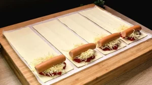 Ein Mini-Würstchen wird auf den mit Käse belegten Blätterteig gelegt