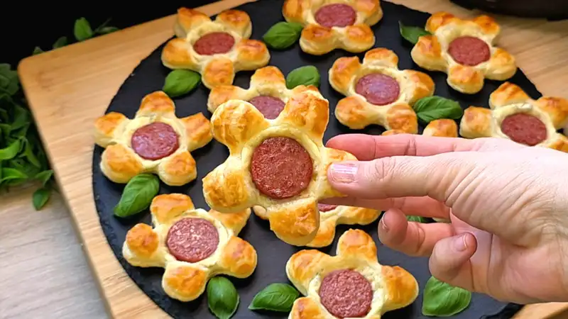 Detailansicht einer würzigen Blätterteigblume mit geschmolzenem Käse und einer Scheibe Cabanossi