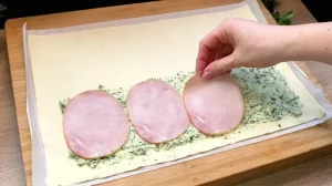 Vier große Scheiben Schinken werden auf die Bärlauch-Käse-Füllung auf dem Blätterteig gelegt.