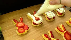 Weiße Schlagsahne wird mit einem Spritzbeutel auf die frischen Erdbeerscheiben im Blätterteig-Hasen dressiert.