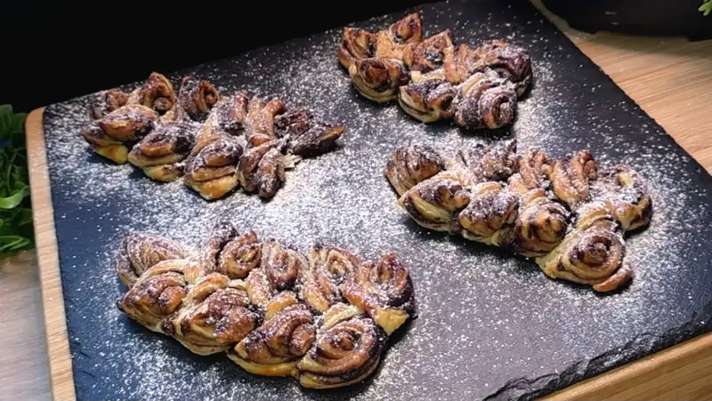 Gebackene Schoko-Weizenähren aus Blätterteig, bestäubt mit Puderzucker auf einem Teller