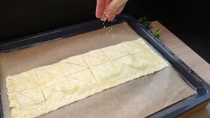 Der eingeschnittene Blätterteig wird vor dem Backen großzügig mit Sesamsamen bestreut.