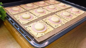 Eine Hand streut Sesamsamen auf die mit Ei bestrichenen Ränder der Blätterteig-Pies.