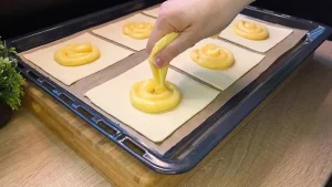 Ein Löffel cremiger Vanillepudding wird mittig auf die Blätterteig-Quadrate gegeben.