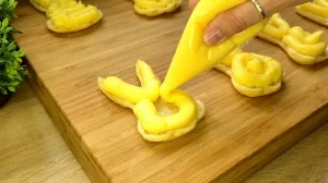 Mit einem Spritzbeutel wird cremiger Vanillepudding in die aufgeschnittenen, gebackenen Blätterteig-Hasen gefüllt.