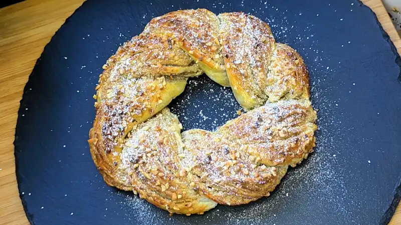 Ein fertig gebackener, goldbrauner Walnusskranz aus Blätterteig auf einem Servierteller