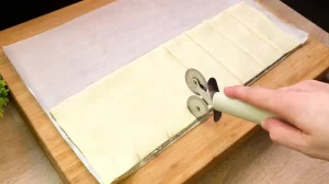 Eine Übersicht der Zutaten: Frischer Blätterteig, Schälchen mit Frischkäse, gehackter Bärlauch, geriebener Käse, Speckscheiben und ein Ei.