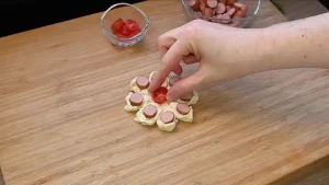 Kleine Tomaten werden in die Mitte von Blätterteig Würstchen Blumen gelegt