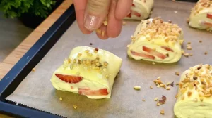 Mit Ei bestrichene Blätterteig Häppchen werden auf dem Backblech mit gehackten Haselnüssen bestreut