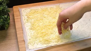 Geriebener Käse wird auf die mit Kräuterfrischkäse bestrichene Teigplatte gestreut