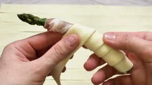 Blätterteigstreifen werden spiralförmig um Spargel mit Speck gewickelt