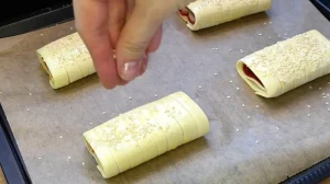 Mit Ei bestrichene Blätterteig Taschen werden auf dem Backblech mit Sesam bestreut