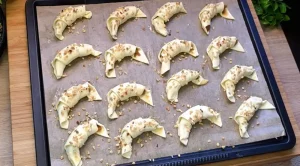 Gefüllte Mini Croissants liegen roh auf dem Backblech und werden vorbereitet