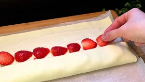 Erdbeerscheiben werden in einer Reihe auf den mit Creme bestrichenen Blätterteig gelegt