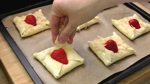 Halbe Erdbeeren werden auf die Teigtaschen gelegt und mit gehobelten Mandeln bestreut