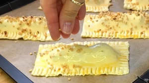 Gehackte Haselnüsse werden auf die mit Ei bestrichenen Riegel auf dem Backblech gestreut