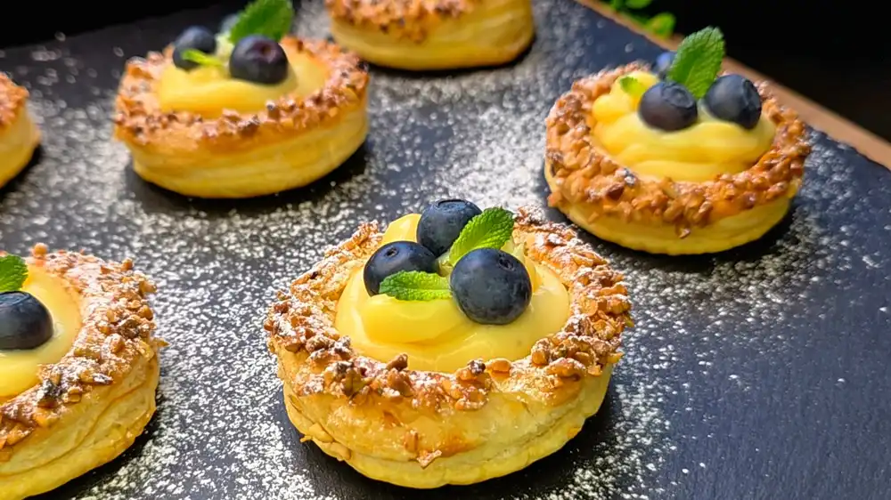 Nahaufnahme von Blätterteig Törtchen mit cremiger Vanillefüllung und frischen Heidelbeeren