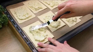Käsecreme wird gleichmäßig auf Blätterteigstücke gestrichen