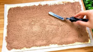 Eine Hand verteilt gleichmäßig gesüßtes Kakaopulver auf einer gebutterten Blätterteigplatte