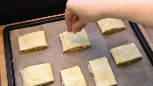 Rohe Pizzataschen auf dem Backblech werden mit Sesamsamen bestreut