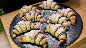Goldbraun gebackene Mohn-croissant aus Blätterteig mit Puderzucker bestäubt auf einem Teller