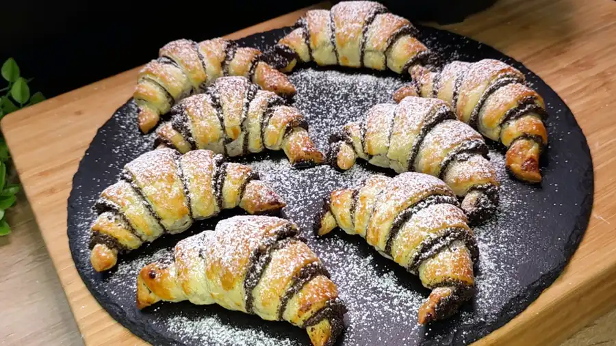 Goldbraun gebackene Mohn-croissant aus Blätterteig mit Puderzucker bestäubt auf einem Teller