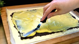 Blätterteig belegt mit einer dunklen Mohnschicht und gelbem Vanillepudding darüber