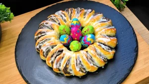 Ein goldbraun gebackener Mohn-Osterkranz aus Blätterteig mit glänzendem Zuckerguss auf einem Ostertisch