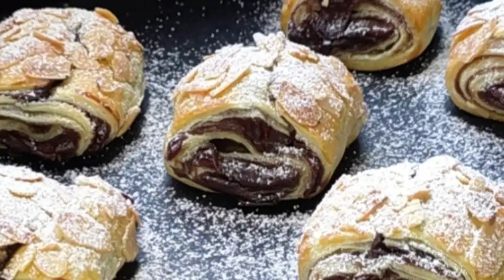 Makro-Aufnahme einer Schokoschnecke mit Puderzucker und Mandelblättchen