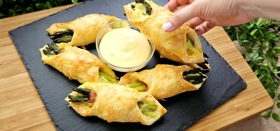 Detailansicht von in Schinken gewickeltem Spargel auf einer Schicht Sauce Hollandaise im Teig