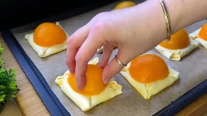 Halbierte Pfirsiche werden auf gefüllten und gefalteten Blätterteig gesetzt