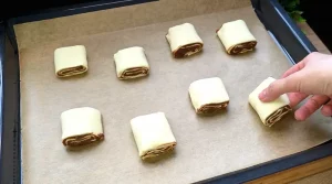 Ungebackene Blätterteigschnecken auf Backpapier, bestreut mit Mandeln