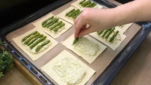 Grüner Spargel wird auf die mit Creme bestrichenen Blätterteigstücke gelegt