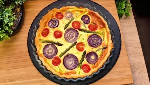 Eine bunte Spargel-Quiche mit Kirschtomaten und roten Zwiebeln in einer Backform