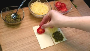 Blätterteig-Quadrat mit Pesto, Käse und einer Tomatenscheibe kurz vor dem Falten