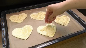Ein rohes Blätterteigherz wird mit Ei bestrichen und mit gehobelten Mandeln bestreut